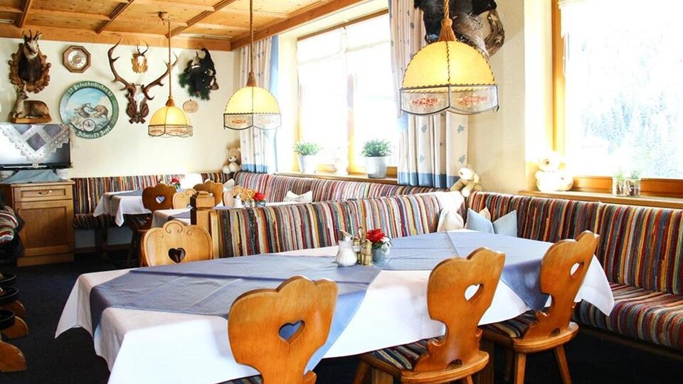 Ein gemütliches Restaurant mit Holzmöbeln und bunten Sitzbänken. Der Raum ist hell und einladend, mit dekorativen Jagdtrophäen an den Wänden.