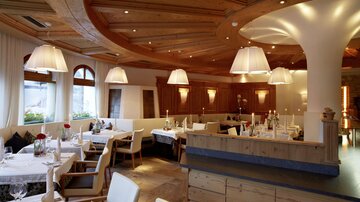 A cozy restaurant with wooden decor and soft lighting. There are tablecloths and flowers on the tables that create an inviting atmosphere.