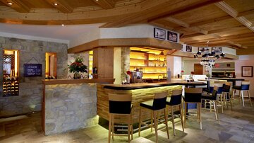 A cozy bar with wooden decor and elegant chairs. The room is brightly lit and invites you to linger.