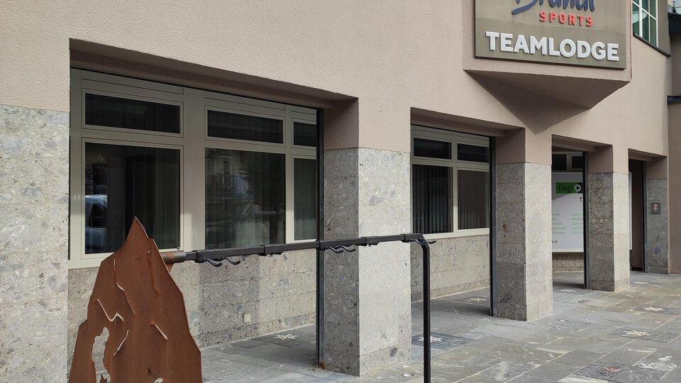 A modern building with a sign that says "Teamlodge." In front of the entrance is another sign featuring sporty motifs.