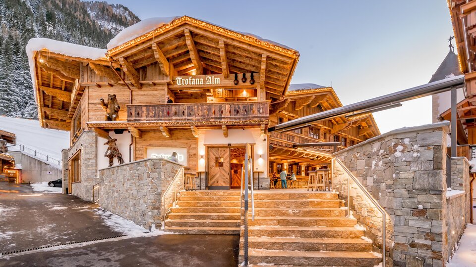 Ein charmantes alpenländisches Gebäude mit Holzstruktur und einem einladenden Eingangsbereich. Der Schnee rund um das Haus sorgt für eine winterliche Atmosphäre.