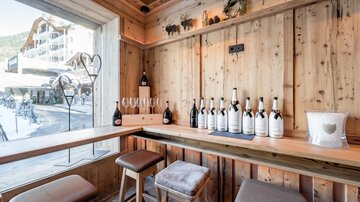 Eine gemütliche Holzbar mit mehreren Flaschen Wein auf dem Tisch. Durch das große Fenster ist ein schöner Blick nach draußen sichtbar.