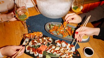 Ein stilvolles Sushi-Dinner mit verschiedenen Sushi-Platten und Cocktails. Im Hintergrund ist eine Flasche Champagner in einem Eiskübel zu sehen.
