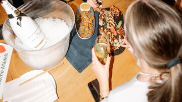 Eine lebhafte Feier in einer Bar mit vielen Menschen. Zwei Frauen lächeln am Tisch, während sie Sushi essen und Drinks genießen.