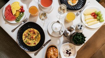 A rich breakfast buffet with fresh fruit, eggs, omelets, and various drinks. The selection is colorful and attractively presented.