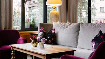 Ein gemütlicher Wohnbereich mit einem hellen Sofa und einem Holzkaffee Tisch. Angenehme Dekoration mit bunten Kissen und einer Lampe sorgt für eine einladende Atmosphäre.