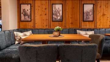 Ein gemütlicher Essbereich mit einer großen, holzverkleideten Wand und stilvollen Bildern. Der Tisch ist mit einer kleinen Blumenvase dekoriert und umgeben von bequemen Sitzgelegenheiten.