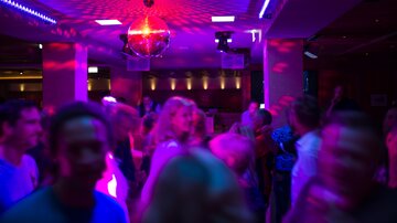 A lively disco with dancing people and colorful lights. A disco ball shines in the background, creating a festive atmosphere.