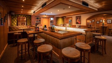 A cozy bar with wooden paneling and warm light. There are seating areas and an inviting atmosphere.
