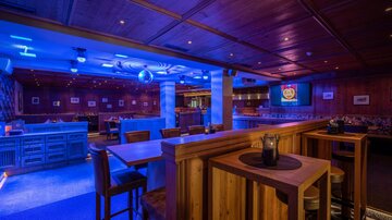 A stylish bar with wooden interior and blue lighting. There are high tables and a relaxed atmosphere.