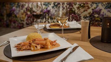 An elegant meal with shrimp and yellow rice on a white plate. In the background, there are wine glasses and a decorative wall.