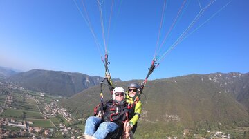 A paragliding experience over a picturesque landscape. The view includes green valleys and mountains under a clear blue sky.