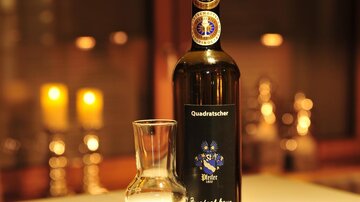 A bottle of fruit brandy is on a table. Next to it are several glasses and in the background, candles are glowing.