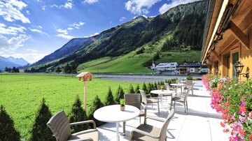 A beautiful terrace with a view of green meadows and mountains. In the background, small houses and a blue sky can be seen.
