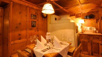 A cozy dining area with wooden walls and warm lighting. The table is elegantly set with glasses and fabric napkins.