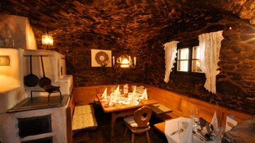A cozy restaurant with stone walls and wooden interior. The table is set rustic style and there is candlelight for an inviting atmosphere.