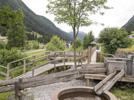 A quiet landscape with a wooden walkway and a water hole. Surrounded by green hills and trees.