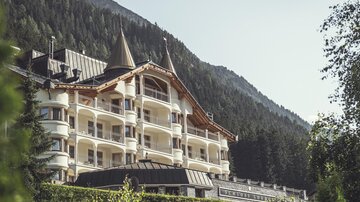 Ein elegantes Hotel mit Türmen, umgeben von grünen Bäumen und Bergen. Die Architektur vereint moderne und alpine Stilelemente. | © Hannes Niederkofler