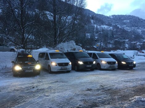 Fünf Taxis stehen in einer schneebedeckten Umgebung. Die Fahrzeuge sind in verschiedenen Farben und warten auf Passagiere.