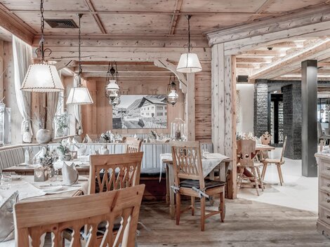 A cozy restaurant with wooden paneling and warm light. There are tables set with elegant tablecloths and wooden chairs.