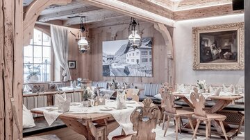 A cozy restaurant with wooden decor and rustic furniture. The tables are nicely set and there are decorative artworks on the walls.