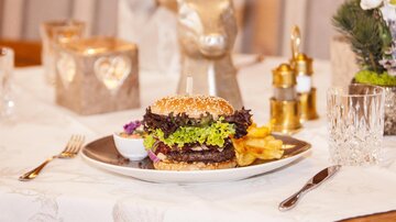 A delicious burger on a plate with fresh salad and fries. The table is elegantly set, with candles and decorative elements in the background.