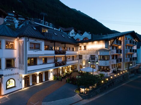 A charming building in alpine style, illuminated at dusk. Surrounded by lush mountains and an inviting atmosphere.