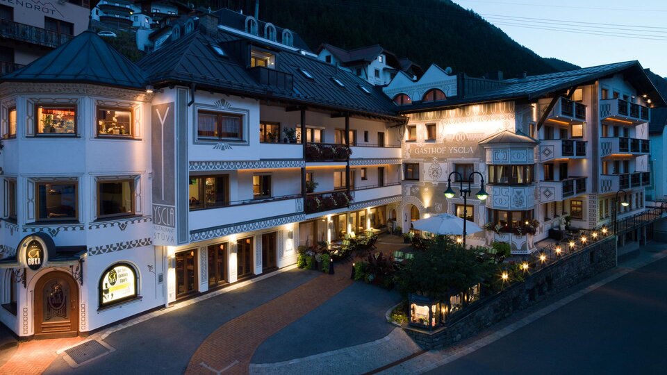 A charming building in alpine style, illuminated at dusk. Surrounded by lush mountains and an inviting atmosphere.