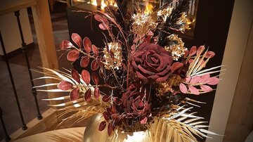 A decorative bouquet of flowers in a golden vase. The composition consists of red roses and various plants that create an elegant atmosphere.
