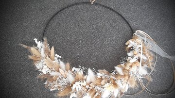 A decorative wreath made of dried flowers and grasses on a black metal ring. It radiates a natural and elegant aesthetic.