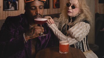 Ein elegante Bar mit zwei Personen. Eine Frau reicht einem Mann ein Getränk, während sie stilvolle Kleidung tragen.