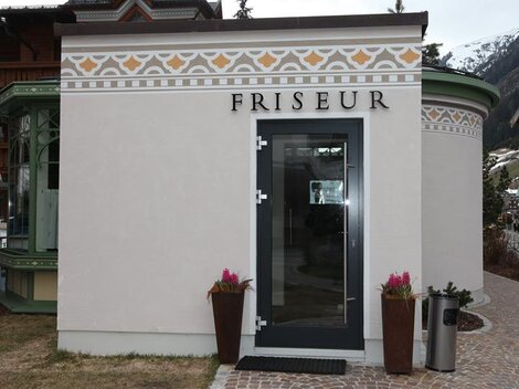 A hair salon with an elegant facade. The entrance door is modern and there are plants on both sides.