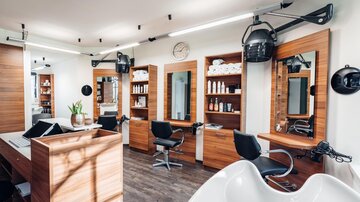 A modern hair salon with wooden shelves and mirrors. There are several barber chairs and a washing station. | © Trofana Royal Resort/valentin_fotoo
