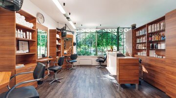 A fresh hair salon with modern chairs and shelves full of care products. Large windows provide plenty of natural light and a view into the greenery. | © Trofana Royal Resort/valentin_fotoo