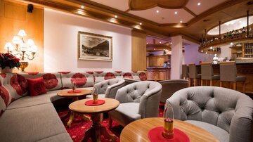 A cozy lounge with gray sofas and a round table. In the background, there is a bar and decorative lighting.
