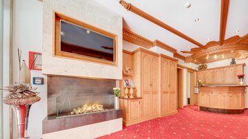 A cozy living room with a modern fireplace and a television. The room is equipped with wooden details and a red carpet.