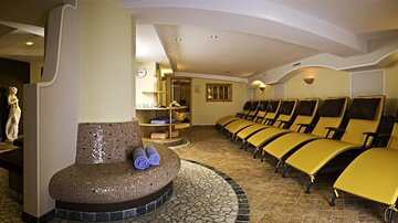A quiet wellness area with comfortable yellow loungers. In the background, there is a reception area and a statuette.