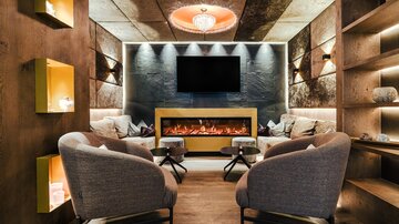 A cozy lounge with modern chairs and an elegant fireplace. The walls are painted in warm tones and accented with atmospheric lighting.