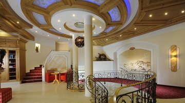 An elegant entrance area with a curved staircase and an intricate ceiling pattern. The room is brightly lit and features stylish furniture and decorations.
