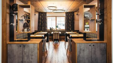 A modern restaurant with wooden elements and stylish shelves. The space is well-lit and offers a view of the outdoor area.