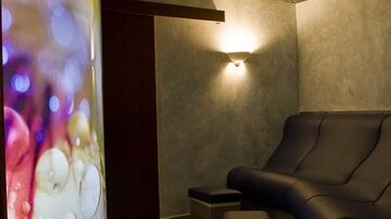 A relaxing space with comfortable seating and soft lighting. On the wall, there is a glowing, colorful projection.