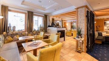 An inviting interior with cozy seating areas and warm colors. Large windows create bright lighting conditions and a pleasant atmosphere.