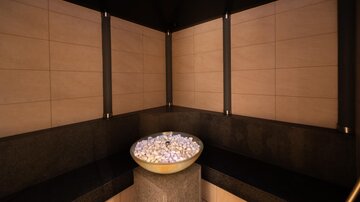 An elegant wellness area with dark walls and soft lighting. In the center, there is a bowl with stones that creates a relaxing ambiance.