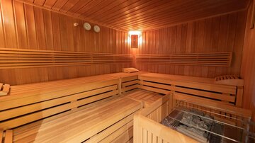 A cozy sauna with wood paneling and benches. A small stove can be seen in the corner.