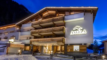 A modern hotel building with wooden cladding and a illuminated facade in a snow-covered environment. The sky is at twilight, and the atmosphere is welcoming.