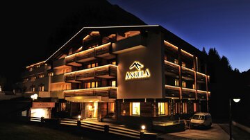 A beautiful hotel building with warm lights at dusk. The facade has elegant balconies and the hotel logo is clearly visible.