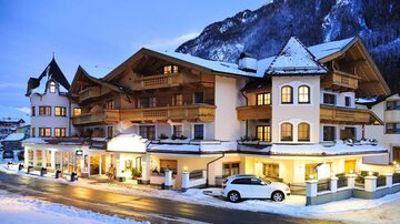 Ein charmantes Hotel im Winter mit schneebedeckten Straßen. Die Fassade ist warm beleuchtet, umgeben von malerischen Bergen.