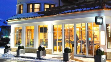 Ein modernes Restaurant mit großen Fenstern in einer verschneiten Umgebung. Es ist Nacht, und die warmen Lichter erhellen die Fassade.