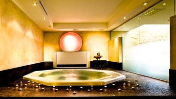 Ein eleganter Wellnessbereich mit einem hexagonalen Whirlpool und sanfter Beleuchtung. Die Wände sind in warmen Tönen gehalten, und Kerzen schaffen eine entspannende Atmosphäre.