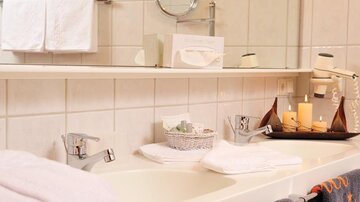 Ein sauberes Badezimmer mit einer Badewanne, weißen Handtüchern und einem dekorativenTablett. Auf dem Tablett stehen Kerzen, ein kleiner Korb und Toilettenartikel.